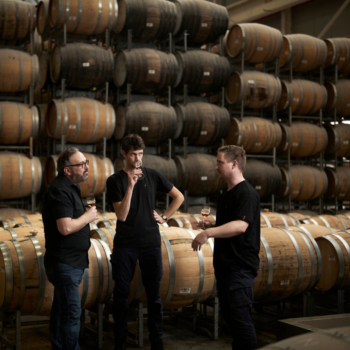 three men tasting whisky barrels distillery wooden glasses whisky liquids gold black uniforms