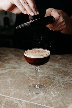 cocktail glass liquids stem black coffee stone counter hands grating garnish powder chocolate foam