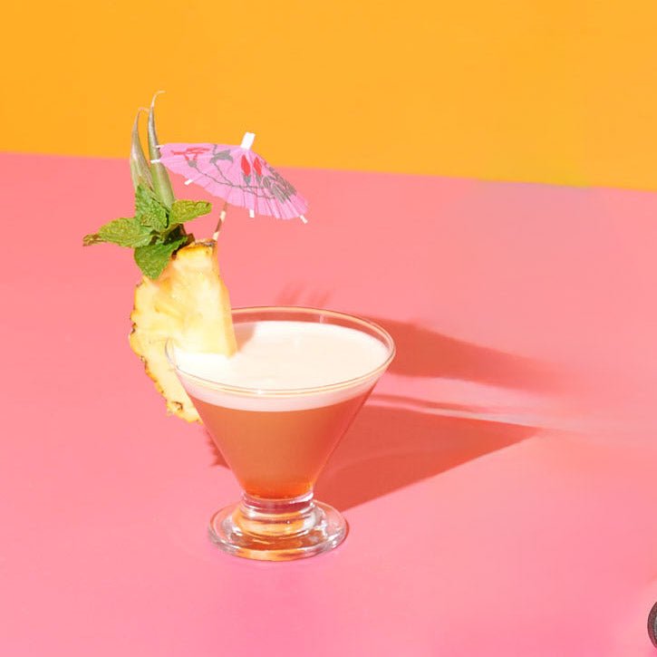 tropical cocktail glass liquid orange pink pineapple fruit mint leaves garnish umbrella foam liquid drink