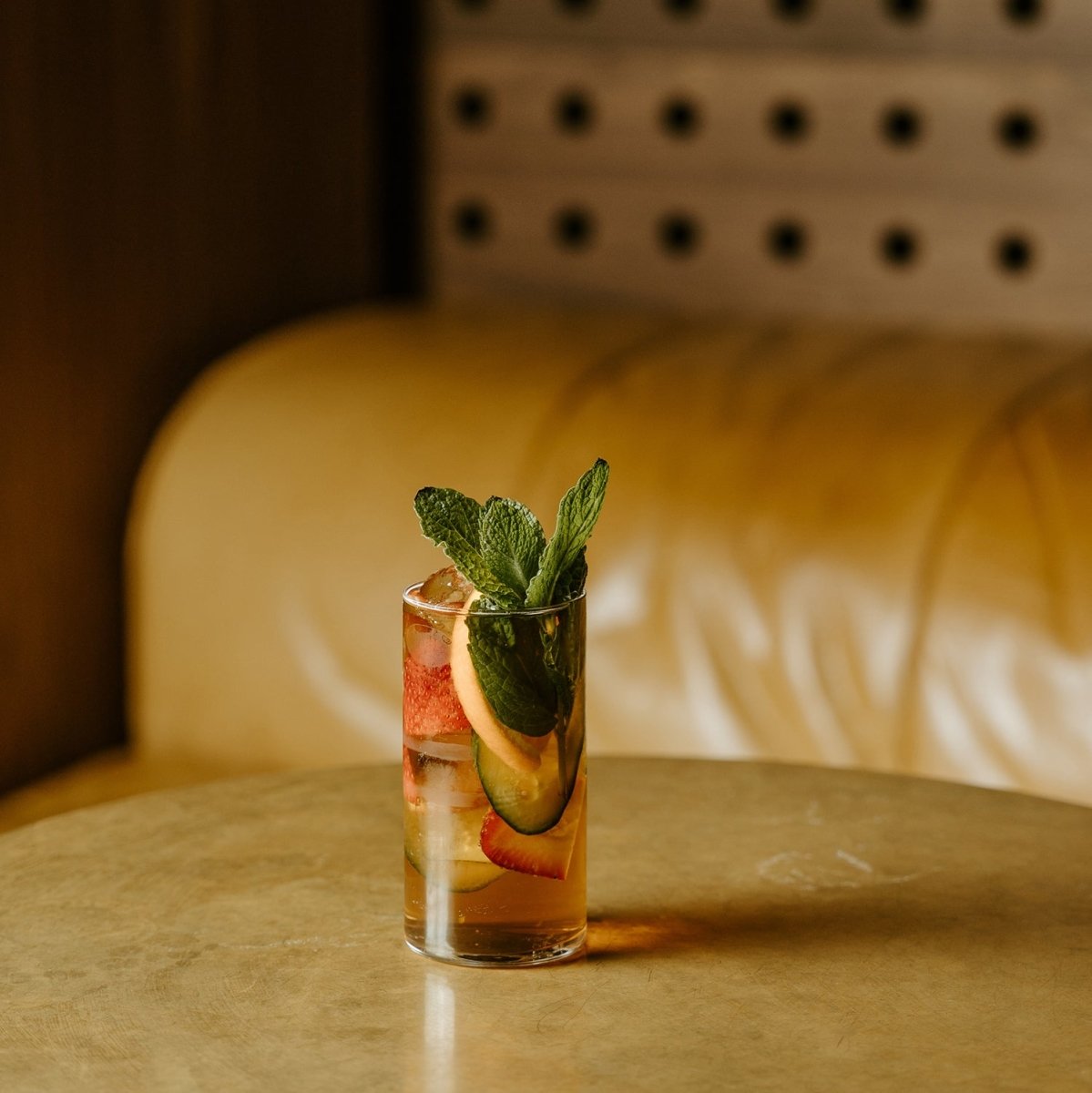 gold couch yellow table cocktail glass liquid fruits cucumber strawberry lemon mint leaves