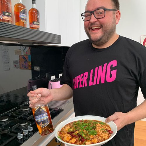 man cooking food holding glass whisky bottle liquid blue label red amber tofu green vegetables