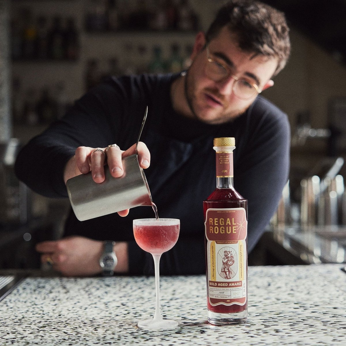 man pouring cocktail tall stemmed glass vermouth red liquid bottle