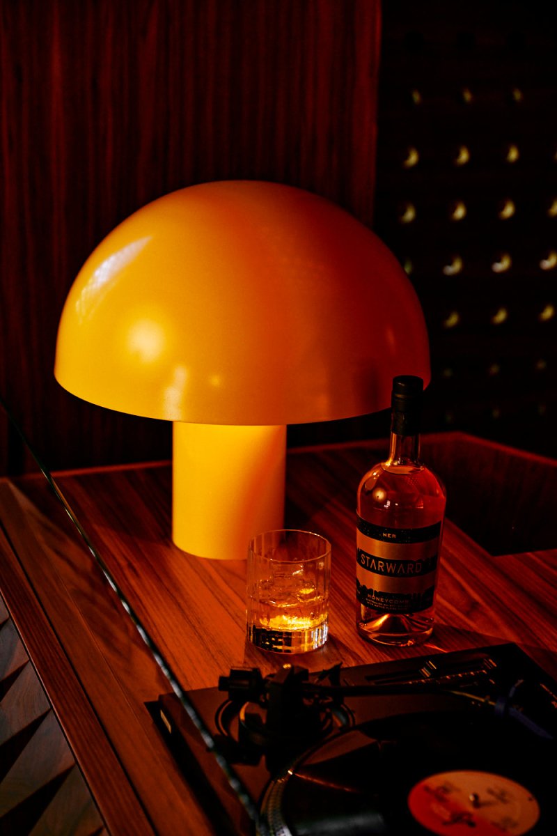 mushroom shape lamp gold orange warm light dark wooden table whisky glass bottle amber liquid cocktail ice record player