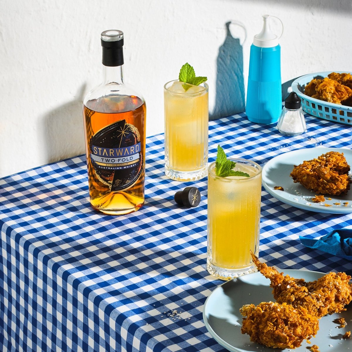 cocktails table tablecloth blue white checkered liquids yellow fizzing fried chicken whisky glass bottle amber liquid