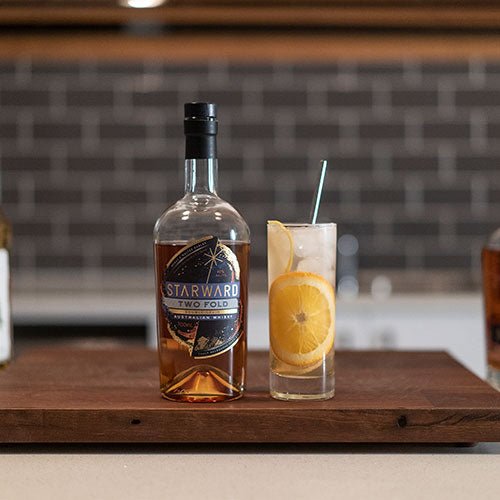 cocktail glass liquids gold yellow wooden counter kitchen grey tiles whisky bottle blue label ice