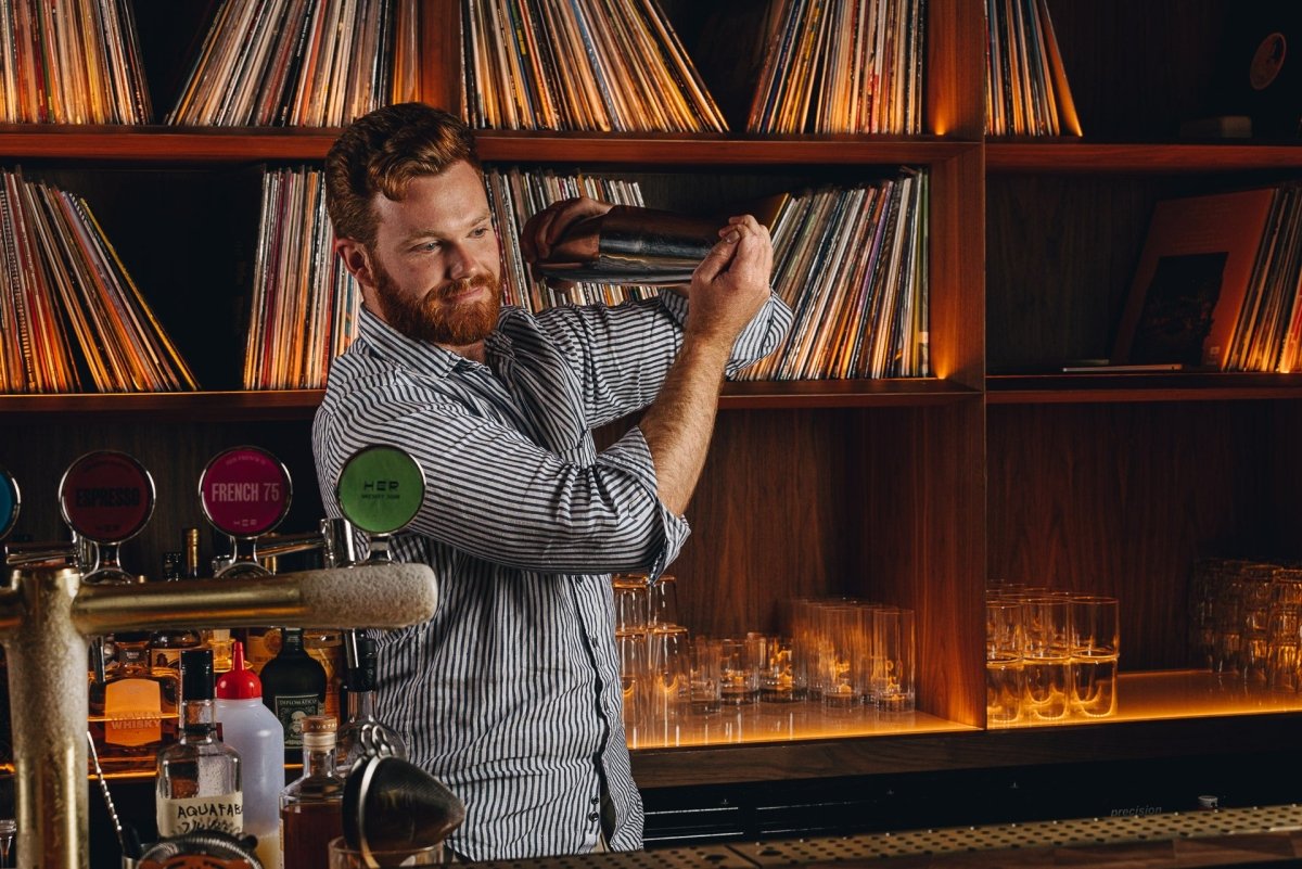 ambient warm room bookshelves records vinyls man shaking cocktail whisky beertaps frost